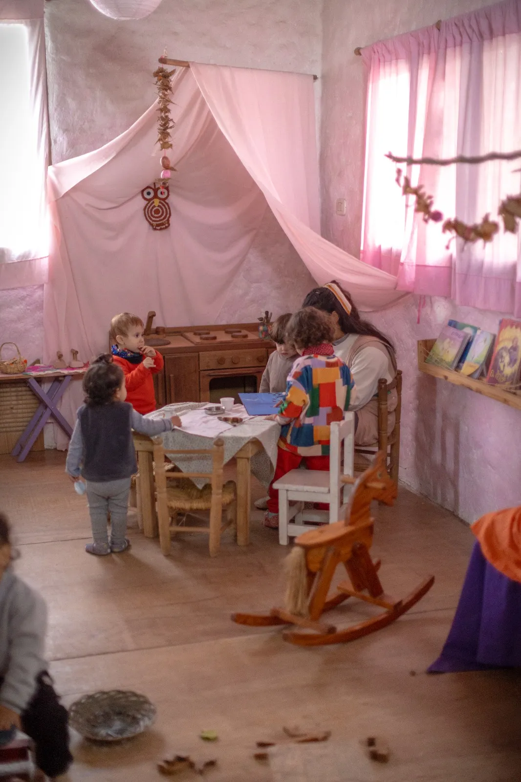 Maestra y niños pequeños jugando junto a una cocinita de madera en una sala cálida del jardín