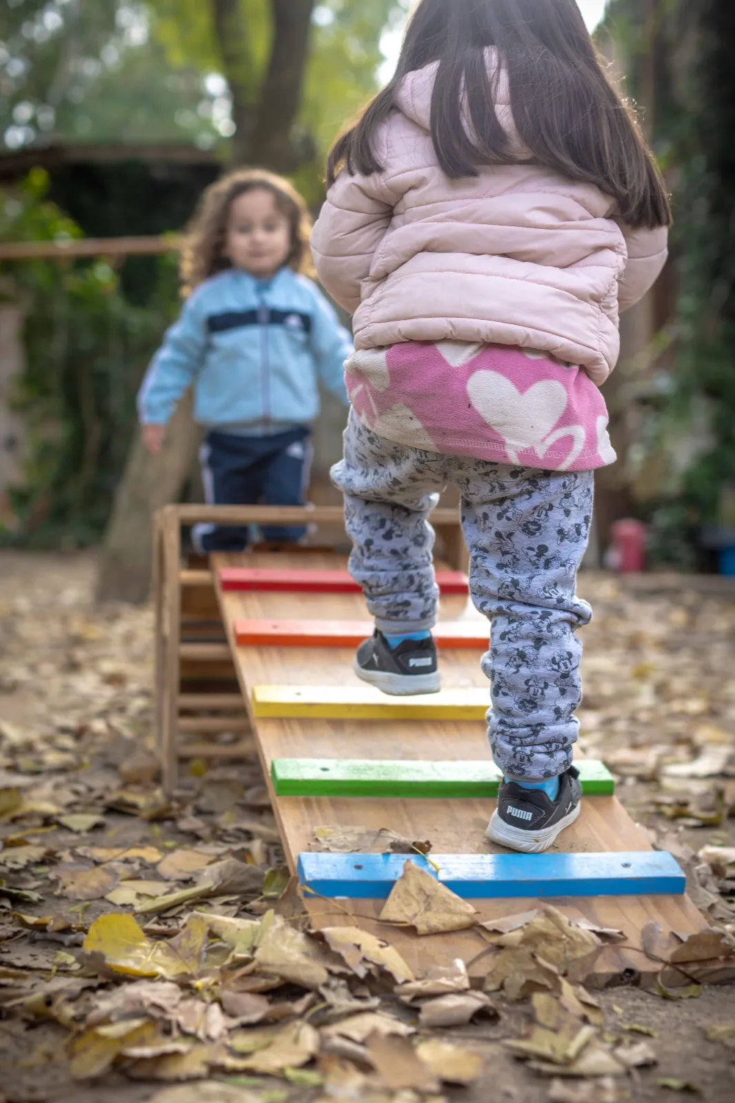 Dos niños caminando sobre un puente de equilibrio de madera con peldaños de colores